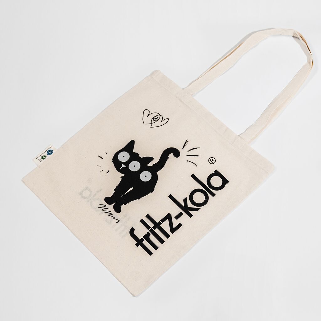 Beige Stoffbeutel mit schwarzen Zeichnungen: dreiäugige Katze und "fritz-kola" Schriftzug. Beutel hat lange helle Tragegriffe.