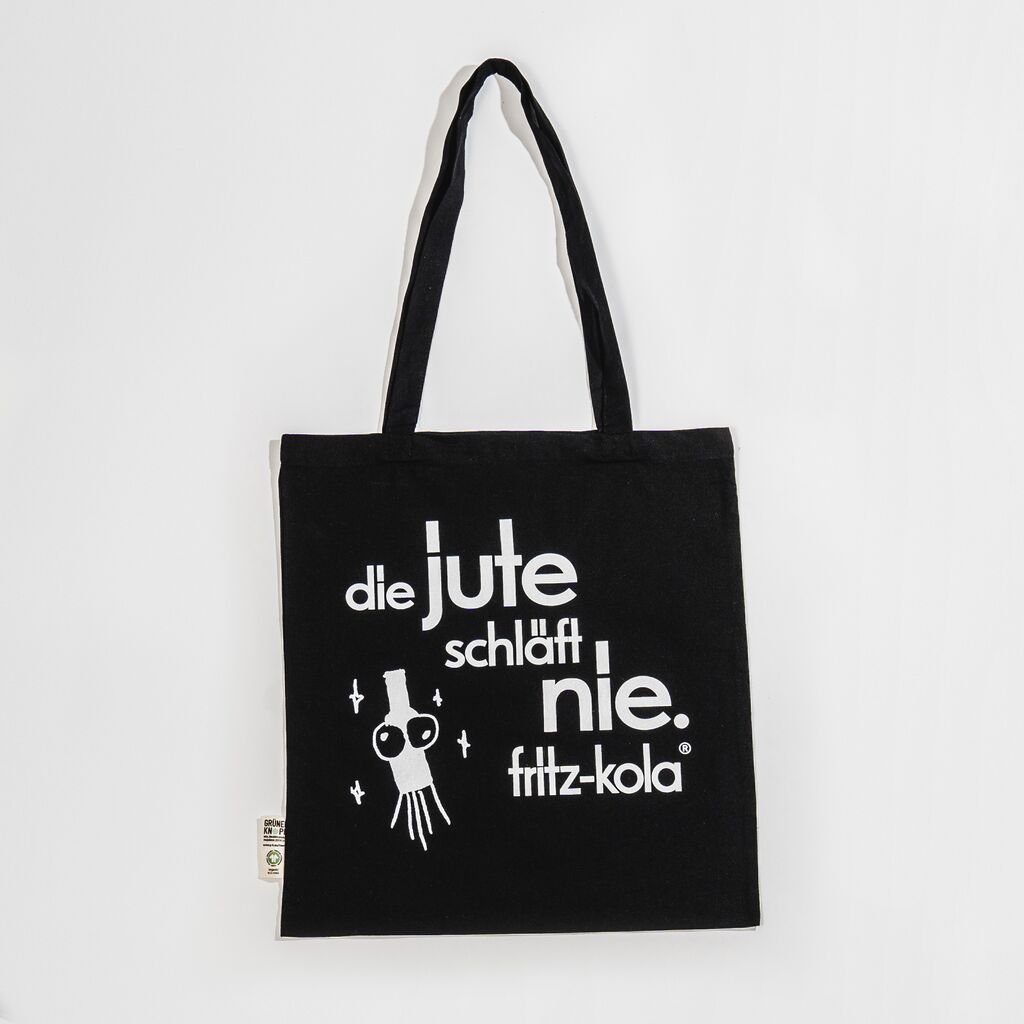 Schwarze Stofftasche mit weißem Aufdruck "die jute schläft nie." und fritz-kola Logo. Links daneben eine stilisierte weiße Flasche und Sternen drumherum.