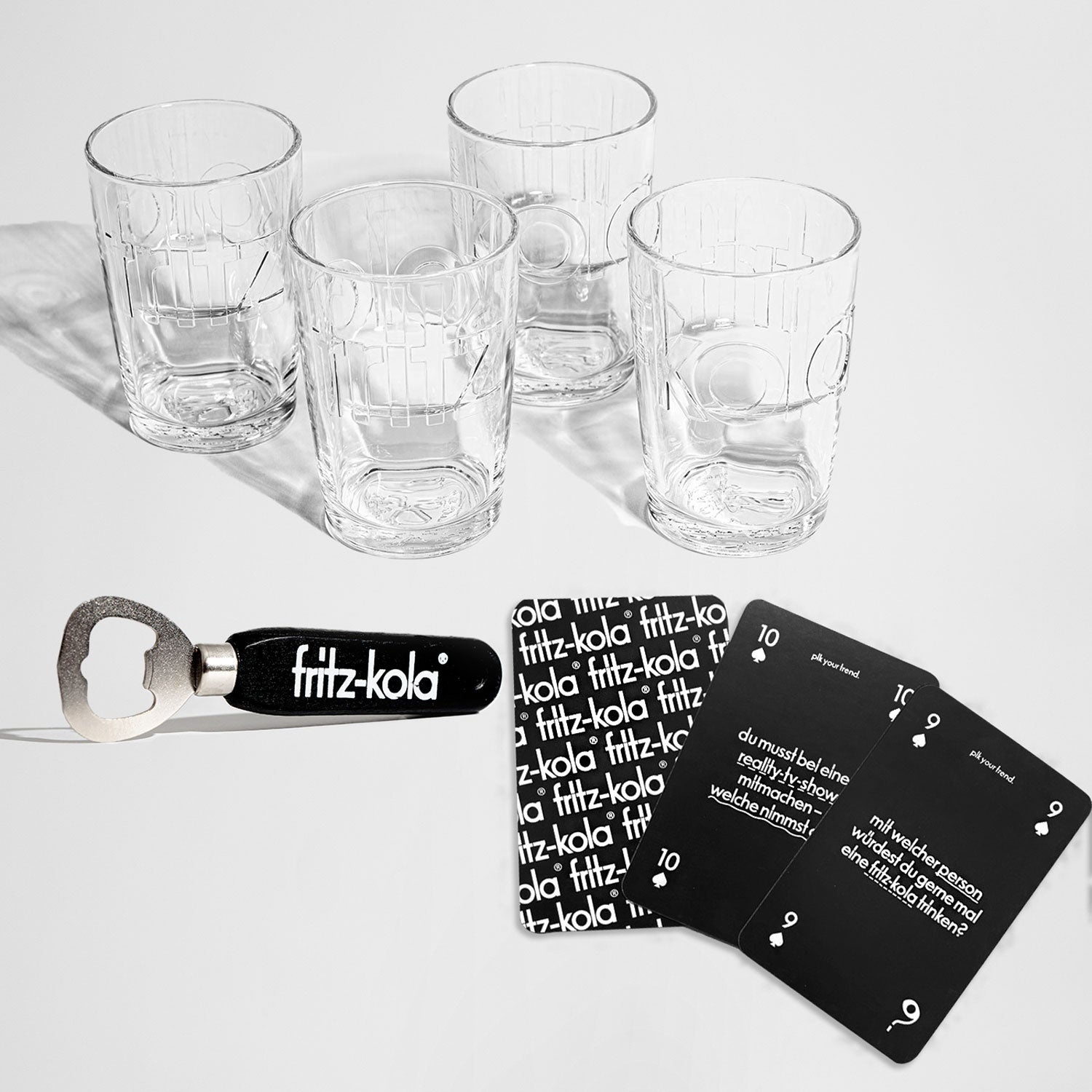 Geschenkset ‚fritz&yap‘ mit vier Gläsern im fritz-kola Design, einem schwarzen Flaschenöffner mit fritz-kola Logo und dem Kartenspiel ‚fritz&yap‘ mit Gesprächsfragen.