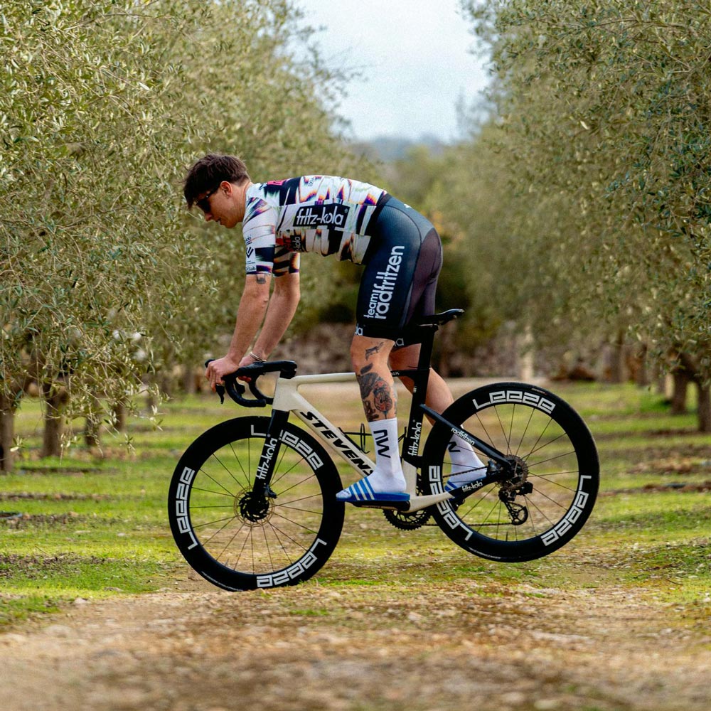 Einzelner Radsportler balanciert in einem Olivenhain  auf weißem Rennrad. Er trägt das radfritzen trikot.