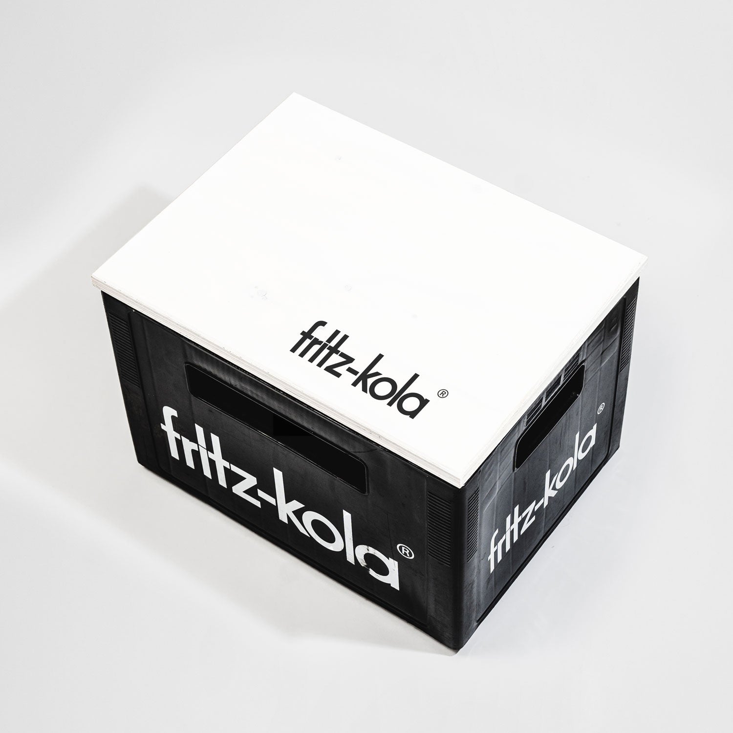 Schwarze fritz-kola Getränkekiste mit weißem Schriftzug an den Seiten, darauf liegt weißer Holz-Deckel mit "fritz-kola" Logo