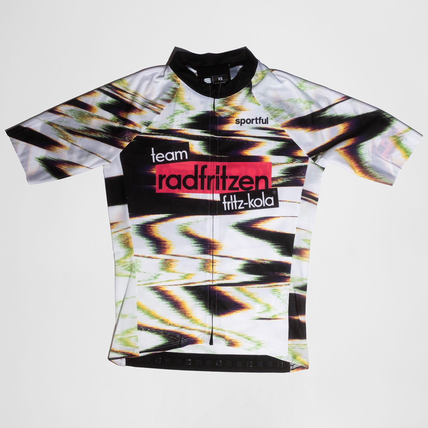 Weißes Radtrikot mit abstraktem Farbverlauf-Muster in Grün, Pink und Schwarz. Zentraler roter Balken mit "radfritzen" auf der Brust, darunter "fritz-kola" Logo. kurze Ärmel, Reißverschluß