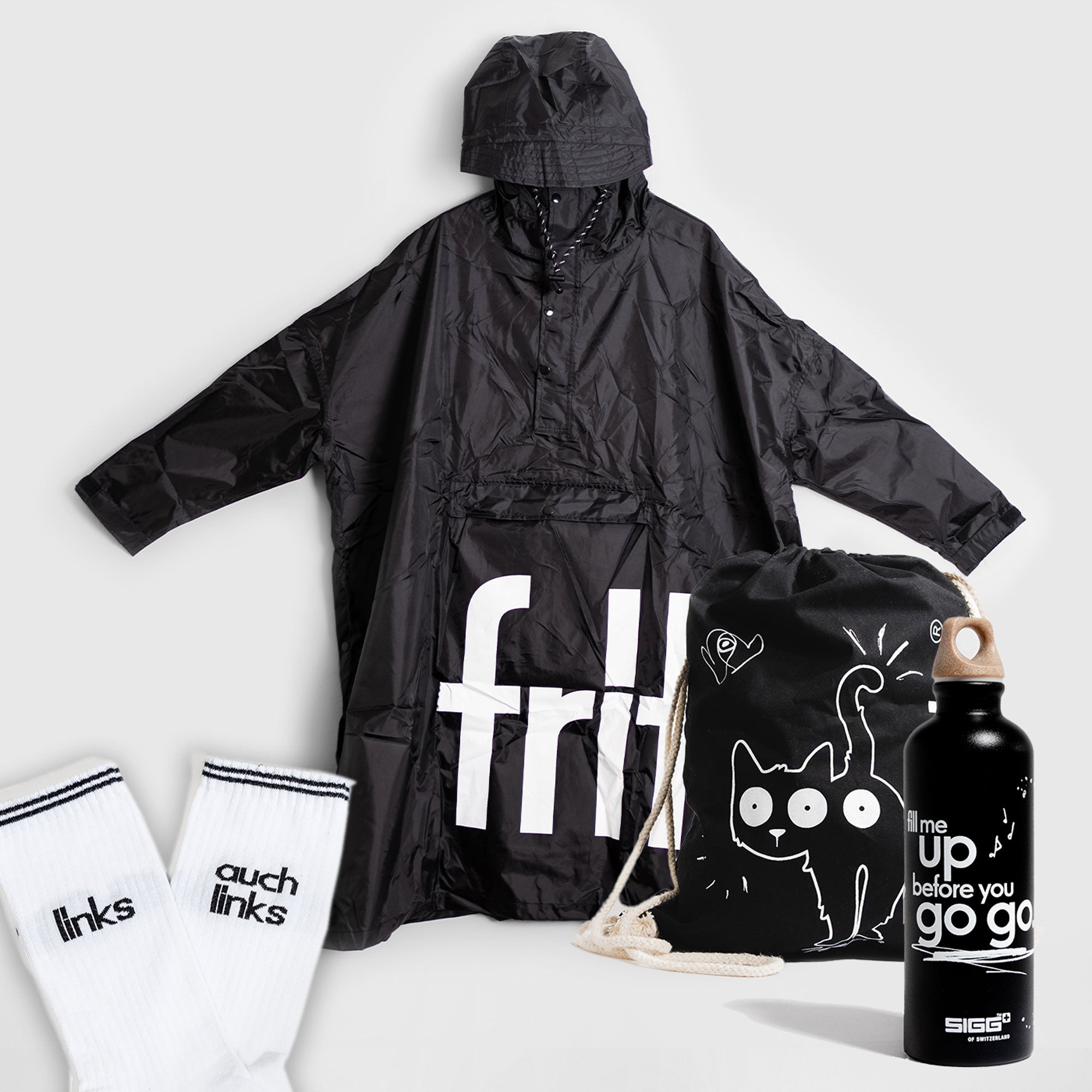 Geschenkset von fritz-kola bestehend aus einem schwarzen Regenponcho mit großem weißen fritz-Logo, einem schwarzen Turnbeutel mit Katzenmotiv, einer schwarzen Trinkflasche mit weißem Schriftzug ‚fill me up before you go go‘ und einem Paar weißer Socken mit schwarzem Text ‚links‘ und ‚auch links‘