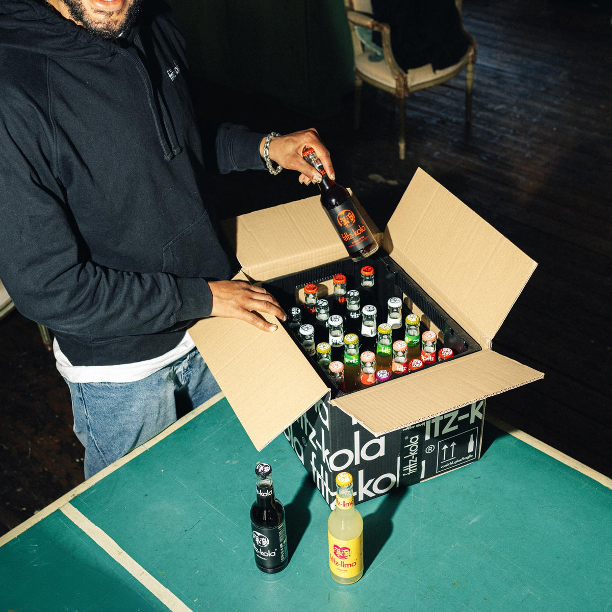 Person packt eine Lieferung von fritz-kola aus und stelle die Flaschen auf eine Tischtennisplatte
