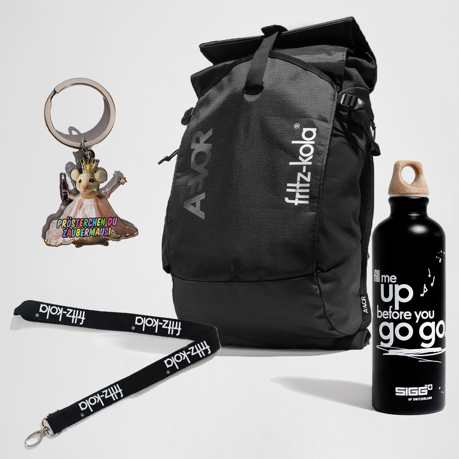 Set aus fritz-kola Merchandise: schwarzer AVOR-Rucksack mit fritz-kola-Logo, schwarze Trinkflasche mit weißem Schriftzug ‚fill me up before you go go‘, Schlüsselanhänger in Form einer Maus mit Krone und buntem Text ‚Prösterchen du Zaubermausi‘ sowie schwarzes Lanyard mit weißem fritz-kola-Schriftzug.