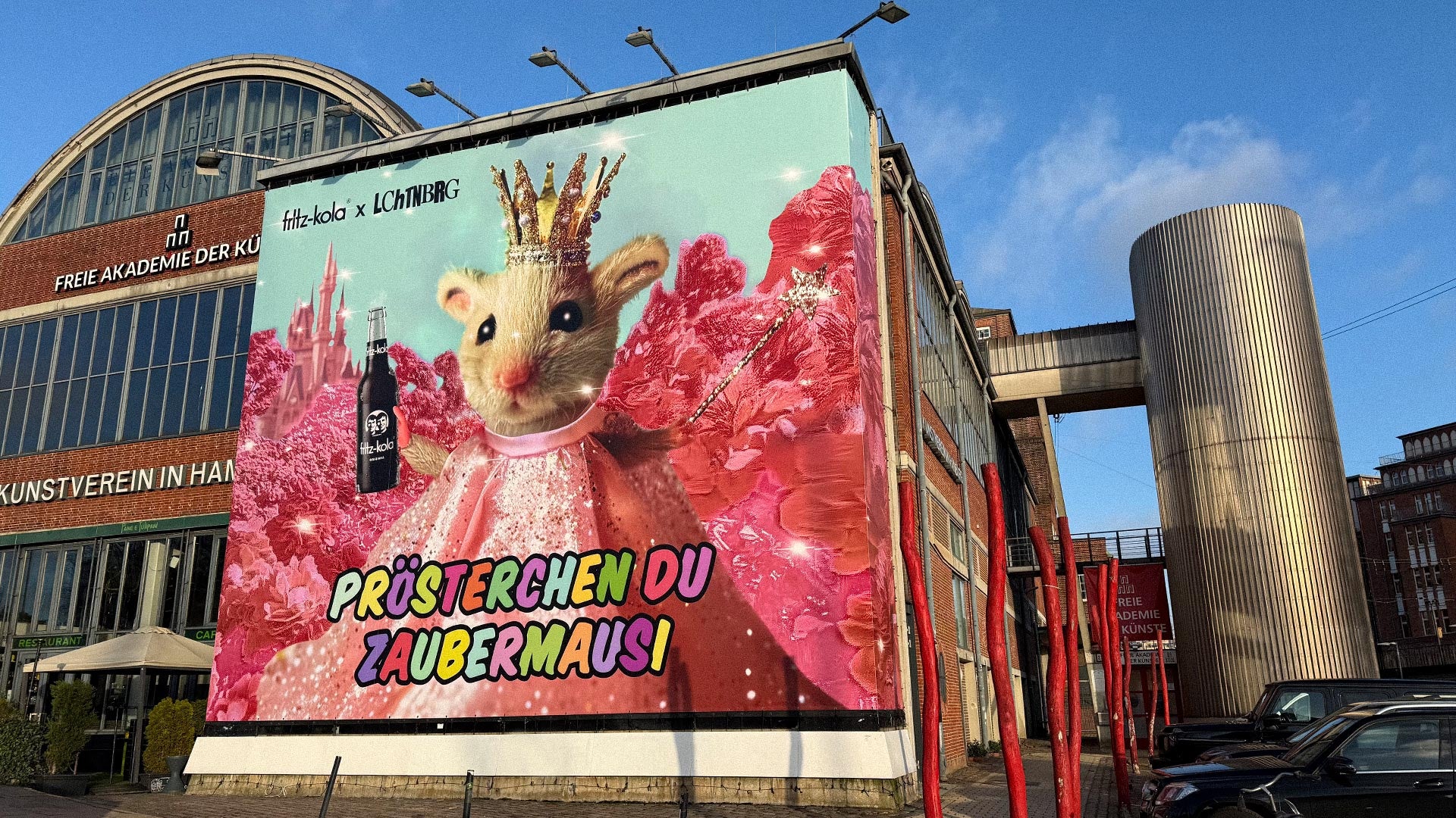 Ein künsterlisches Plakat von fritz-kola in Kooperation mit dem Künstler LCHTNBERG auf der Werbefläche vom Kunstverein Hamburg. Das Plakat zeigt eine Maus mit einer fritz-kola Flasche in der Hand und einem Zauberstab. Sie trögt eine Krone und ein pinkes Kleid. Darunter steht "prösterchen du zaubermausi"